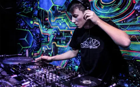 Młody DJ w słuchawkach miksuje muzykę na tle psychodelicznej, neonowej ściany. Chcesz wiedzieć, jak zostać DJ-em? Zacznij od tego!