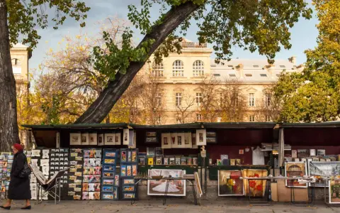 Ein Stand auf dem **Flohmarkt Paris** mit Postkarten, Büchern und Gemälden vor einem historischen Gebäude.