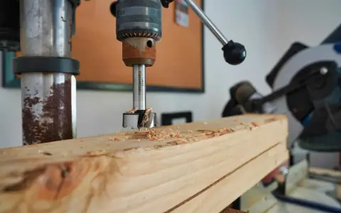 Trapano a colonna che fora un pezzo di legno, creando trucioli. Un esempio pratico di come avvitare una vite nel legno, o meglio, preparare il foro.