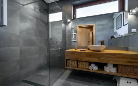 Salle de bain moderne avec douche à l'italienne, carrelage gris, meuble en bois et vasque. Le pose carrelage douche italienne est impeccable.