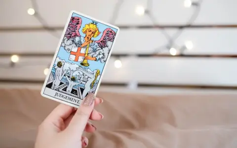 Una mano sostiene la carta de **el juicio tarot**, mostrando un ángel con trompeta y personas resucitando.