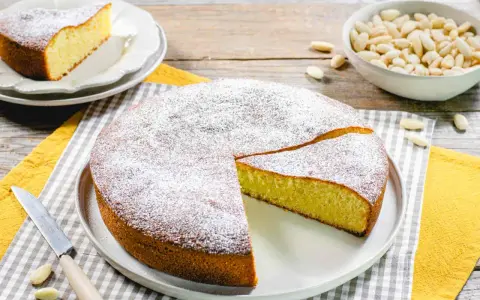 Una deliziosa torta con farina di mandorle, spolverata di zucchero a velo, pronta per essere gustata. Accanto, una ciotola di mandorle intere.