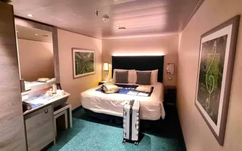 Interno di una royal caribbean cabine con letto matrimoniale, specchio, scrivania e valigia pronta per il viaggio.