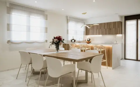 Elegantes cocinas abiertas al salón con barra, mesa de comedor y sillas blancas.