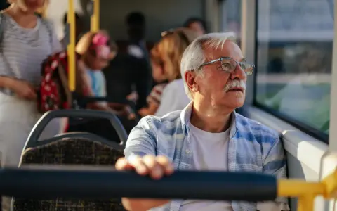 Starszy pan w okularach podróżuje autobusem, ciesząc się darmową komunikacją miejską.