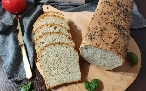 Świeżo upieczony chleb pszenny z makiem, pokrojony w kromki, obok pomidor i złoty nóż.