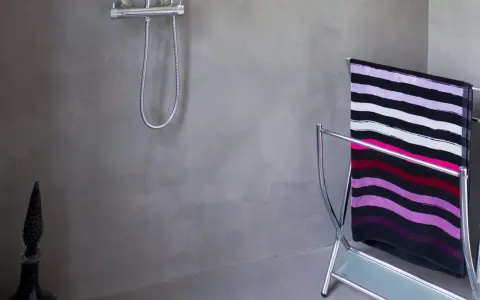 Salle de bain béton ciré aux tons gris, avec une douche chromée et un porte-serviettes orné d'une serviette rayée.