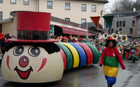 Bunter Karnevalsumzug mit einem riesigen Clown-Motivwagen und kostümierten Menschen. Die Karnevalstage sind voller Freude und bunter Kostüme.