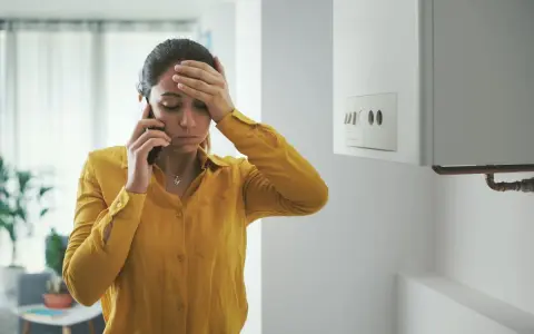 Donna preoccupata al telefono vicino allo scaldabagno, cerca consigli su come evitare il calcare.