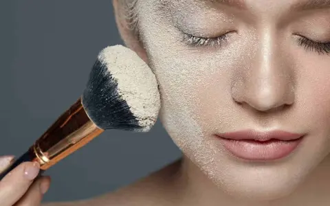 Applicazione di cipria per il baking trucco su un viso, con un pennello carico di prodotto.