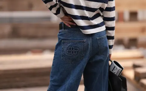 Kobieta w granatowych jeansach z logo i bluzce w paski. Idealne spodnie dla niskich kobiet, które podkreślą sylwetkę.