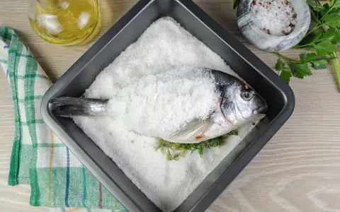 Dorada a la sal lista para hornear, con hierbas frescas y aceite de oliva al lado.