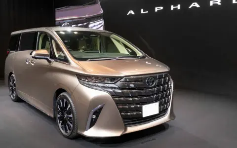 Brązowy minivan Toyota Alphard na ciemnym tle, z widocznym napisem "ALPHARD".