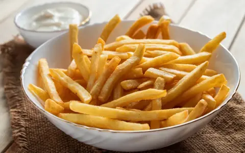 Chrupiące frytki z airfryer w białej misce, obok sos. Idealna przekąska na szybki obiad.