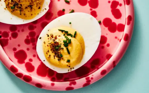 Deviled eggs deutsch: halbe hartgekochte Eier mit cremiger Füllung, bestreut mit Schnittlauch und Gewürzen, auf einem pinkfarbenen Teller mit roten Tupfen.