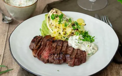 En saftig grillad ryggbiff serveras med krispig sallad, grillad kål och en krämig sås.