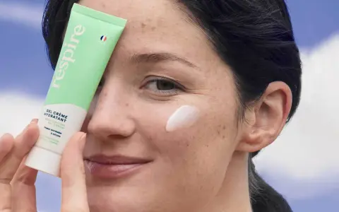 Une femme applique une crème hydratante sur sa joue. Une solution pour comment hydrater sa peau très sèche.