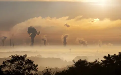 Dymiące kominy fabryk tworzą kłęby, które przypominają, jak wygląda chmura radioaktywna, unosząc się nad mglistym krajobrazem o wschodzie słońca.
