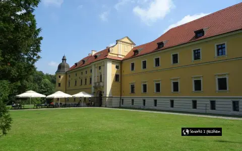 Żółty pałac z czerwonym dachem, gdzie można usiąść pod parasolami. W oddali widać drzewa, a na trawniku rozłożono stoliki. To miejsce, gdzie można poczuć atmosferę rudy raciborskie.