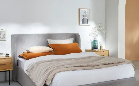 Cama gris con cojines naranjas y beige, perfecta para organizar canapé y crear un ambiente acogedor.