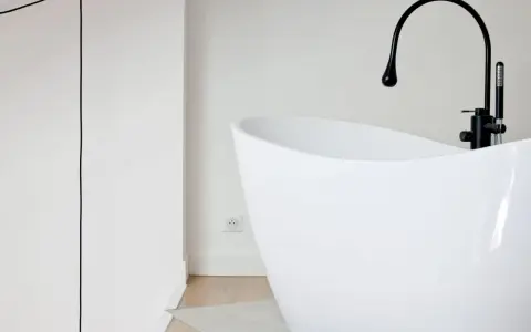 Baignoire îlot blanche au design moderne, avec robinetterie noire. Sa forme suggère une largeur baignoire standard, idéale pour un confort optimal.