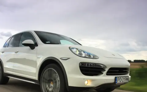 Biały Porsche Cayenne 2025 pędzi po drodze, chmury na niebie sugerują dynamiczną podróż.