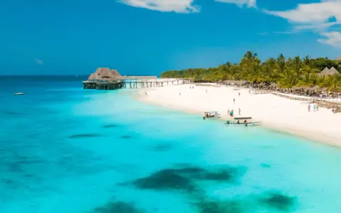 Piękna plaża na Zanzibarze, gdzie ludność cieszy się słońcem i turkusową wodą. Widać łodzie i palmy.