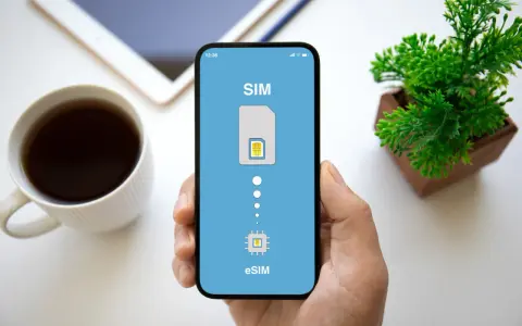 Dłoń trzyma smartfon z ekranem pokazującym proces aktywacji eSIM. Obok kubek kawy i roślinka.