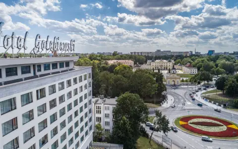 Widok na hotel Gołębiewski w Łodzi z charakterystycznym neonem. W tle rozciąga się miasto z zielenią i budynkami.