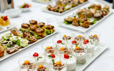 Varietà di antipasti freddi per buffet: mini hamburger, tartine con uova e salumi, e dolcetti in bicchiere con frutta e yogurt.