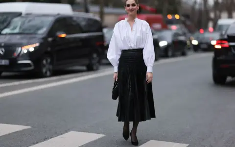 Chic Frau in weißer Bluse und schwarzem oberteil zu plisseerock, steht auf Zebrastreifen.