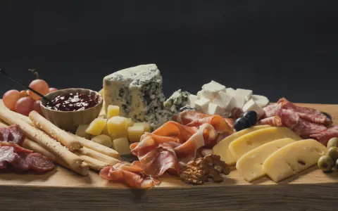Apetyczna taca serów: pleśniowy, żółty, biały, wędliny, winogrona, oliwki, orzechy i dżem.