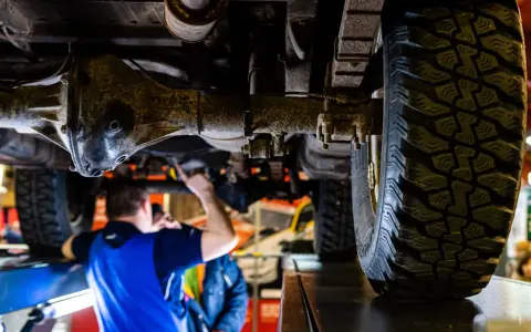 Mechanik sprawdza podwozie terenowego auta z napędem **awd**. Widoczna jest masywna oś i bieżnik opony.