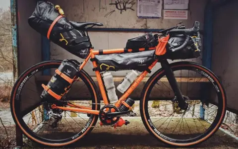 Orange Rennrad mit Bikepacking-Taschen, bereit für Abenteuer.