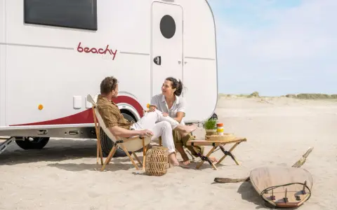 Para na plaży przy kamperze, relaksująca rozmowa. To właśnie karawaning co to – wolność i przygoda.