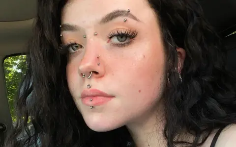 Dziewczyna z licznymi kolczykami: w nosie, ustach, brodzie i na czole. Wyróżnia się anti eyebrow piercing.