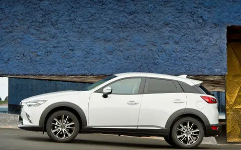 Biała Mazda CX-3 na tle niebieskiej ściany. Sprawdź aktualną mazda cx3 cena i wybierz swój wymarzony samochód.