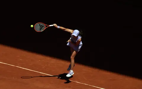 Tenisistka w skoku serwuje piłkę na korcie ziemnym podczas Roland Garros.