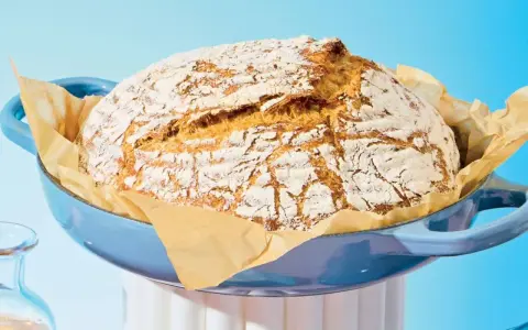 Pain maison doré dans une cocotte bleue, prêt à être dégusté. Le temps de cuisson pain 500g est parfait pour cette croûte craquelée.