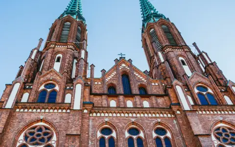 Dwie wieże ceglanego kościoła z zielonymi iglicami, jeden z najpiękniejszych kościołów w Polsce, pod błękitnym niebem.