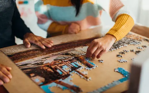 Dwie osoby składają puzzle, tworząc obraz. To dowód na to, że najlepsi producenci puzzli tworzą dzieła, które łączą ludzi.