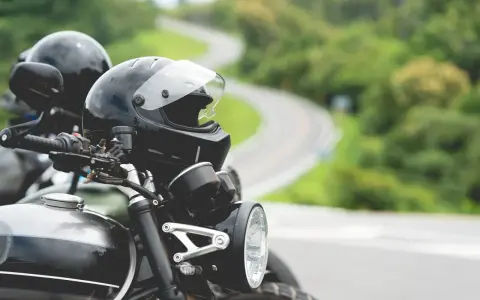 Gotowe na przygodę? Zastanawiasz się nad prawem jazdy na motor i wiekiem? Dwa kaski czekają na motocyklistów na krętej drodze.