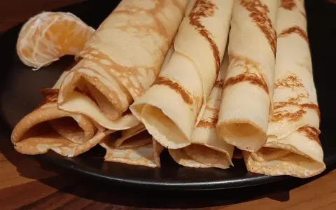 Crêpes à la bière roulées, dorées et légères, servies sur une assiette noire avec un quartier d'orange. Un délice !