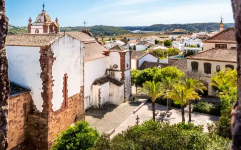 Blick über die weißen Häuser und Palmen von Silves, Portugal, mit einer Kirche im Vordergrund.