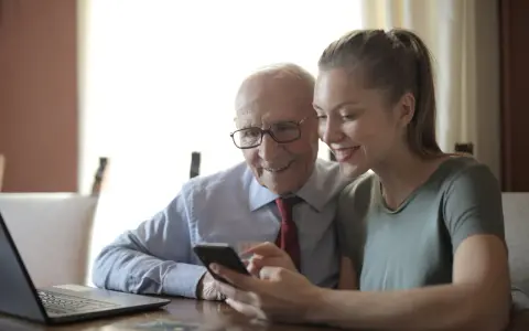 Starszy pan i opiekunka patrzą na telefon, dyskutując o tym, ile zarabia opiekunka osób starszych na godzinę.