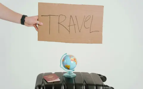 Ręka trzyma tabliczkę z napisem TRAVEL. Obok walizka, globus i paszport. Czy to zapowiedź kolejnych pozytywnych emka travel opinie?