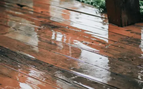 Pluie sur un bois brun, saturateur pas sec, créant des reflets et des ronds dans l'eau.
