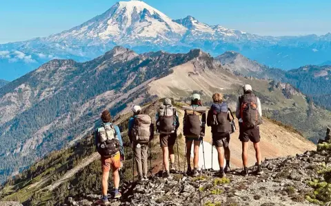 Sześcioro turystów z plecakami na grani, podziwiających majestatyczny szczyt góry na tle błękitnego nieba. To piękny widok z Pacific Crest Trail.