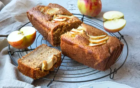 Saftiger Apfelkuchen mit Apfelmus-Note, dekoriert mit frischen Apfelscheiben. Daneben liegen Äpfel und ein Stück Kuchen.