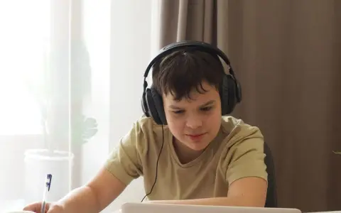 Chłopiec w słuchawkach uczy się zdalnie, notując. Dopełnienie odpowiada na pytania: kogo? czego? komu? czemu? kogo? co? czym? kim? o kim? o czym?